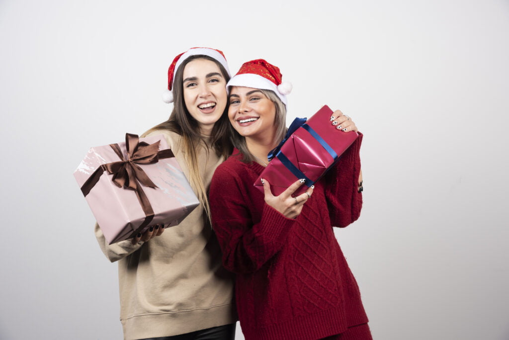 25+ Ide Hadiah Natal untuk Teman Kerja - two smiling girls santa hat holding festive christmas presents 10 Rekomendasi Hadiah Natal untuk Teman Kantor
hadiah natal untuk teman kerja